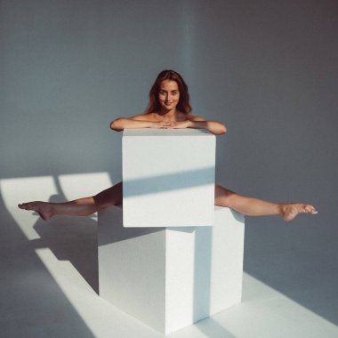 Plastik figürlü genç bir kız, stüdyoda beyaz küpleri yalıyor, plastikleri gevşetiyor, pencereden gelen güneş ışığı onun üzerinde parlıyor..