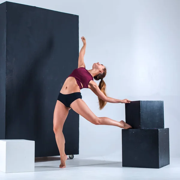 A young girl, a gymnast, with a plastic figure, makes plastic eases on cubes in the studio, sunlight from the window shines on her.