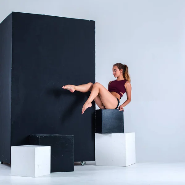 A young girl, a gymnast, with a plastic figure, makes plastic eases on cubes in the studio, sunlight from the window shines on her.