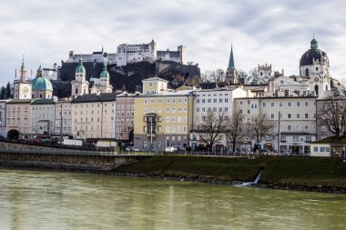 Salzburg, Avusturya - 5 Mart 2017: Üniversite Kilisesi ve Arkaplanda Hohensalzburg Kalesi ile Salzach Nehri manzarası