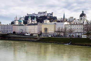Salzburg, Avusturya - 5 Mart 2017: Üniversite Kilisesi ve Arkaplanda Hohensalzburg Kalesi ile Salzach Nehri manzarası
