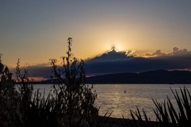 Gelendzhik tatil beldesi, deniz ve dağların kumlu plajında, bulutların ardında alevli bir günbatımı. Karadeniz kıyısı