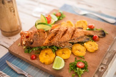 Kızarmış balığın yanında sebze ve meyve bir restorandaki ahşap masada servis edilir.