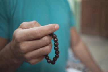 Açık havada meditasyon yaparken elinde çakra bileziği olan bir adamın eline odaklan.