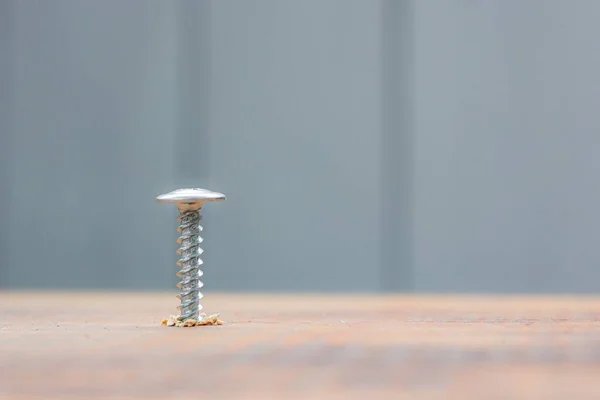 Parafuso de metal branco aparafusada na superfície da placa de madeira escura com chave de fenda. conceito de reparação em casa ou oficina — Fotografia de Stock