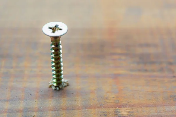 El tornillo de metal tripulado en la superficie del tablero de madera con destornillador. concepto de reparación del hogar o taller —  Fotos de Stock