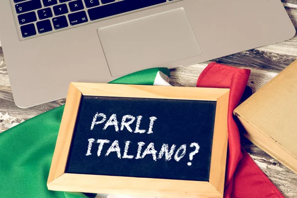 A computer, flag of Italy and a chalk board with the question. Do you speak Italian