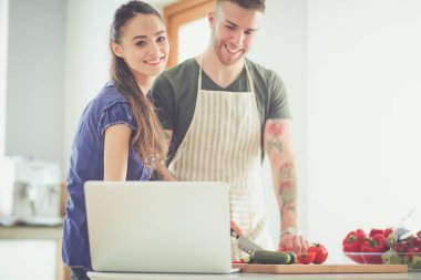 Sebze doğrayan genç bir adam ve mutfakta dizüstü bilgisayarı olan bir kadın.