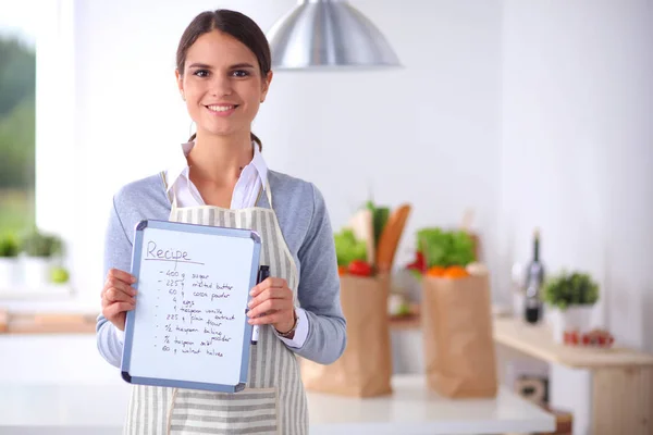 Kvinna i köket hemma, stående nära skrivbord med mapp — Stockfoto