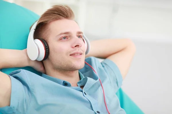 Een jonge knappe man op de bank luisterend naar muziek — Stockfoto