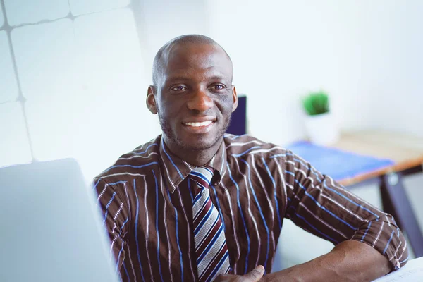 Красивый афро-американский бизнесмен в классическом костюме пользуется ноутбуком и улыбается во время работы в офисе — стоковое фото
