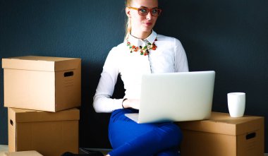 Kadın yerde dizüstü bilgisayarlı bir kutunun yanında oturuyor. .