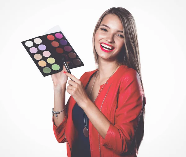 Jeune belle femme tient dans une main et une palette avec de la peinture et des ombres pour le maquillage, brosse d'occasion pour le maquillage — Photo