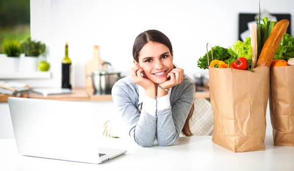 Mooie jonge vrouw koken op zoek naar laptop scherm met ontvangst in de keuken — Stockfoto