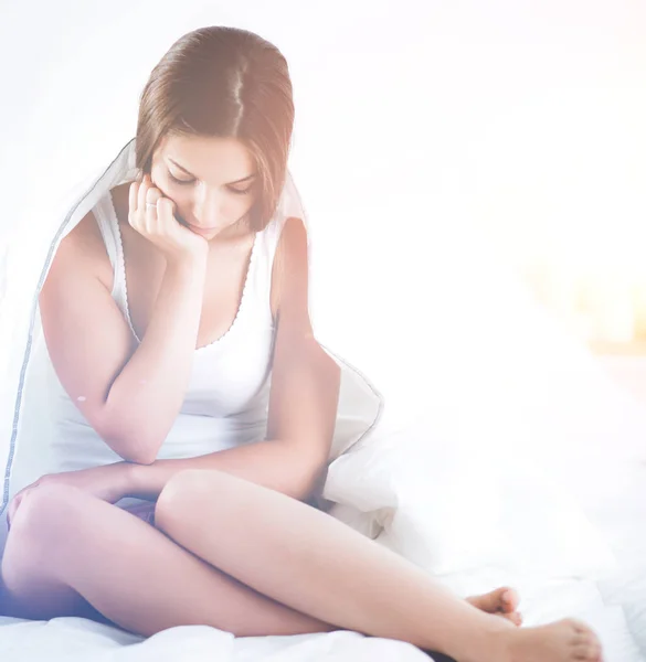 Una hermosa joven sentada en la cama a cubierto —  Fotos de Stock