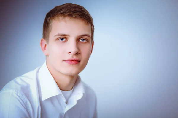Portret van de jonge man die lacht zittend op een grijze achtergrond. Portret van jonge man — Stockfoto