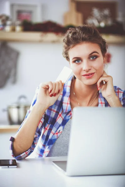 Lachende vrouw online winkelen met behulp van computer- en credit card in keuken. Lachende vrouw — Stockfoto