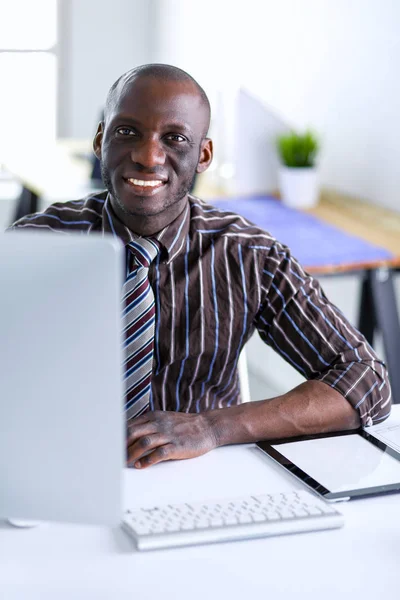 在经典西装的英俊非裔美国商人是使用一台笔记本电脑和微笑在办公室工作的时候 — 图库照片