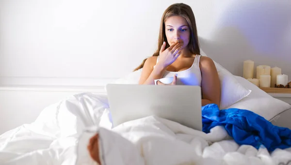 Bardzo młoda kobieta z laptopa w łóżku i cieszyć się filiżanką herbaty — Zdjęcie stockowe