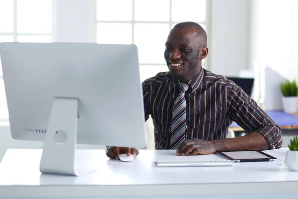 Guapo afroamericano hombre de negocios en traje clásico está utilizando un ordenador portátil y sonriendo mientras trabaja en la oficina — Foto de Stock