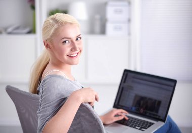 Genç ve güzel bir kadın evde dizüstü bilgisayar kullanıyor.