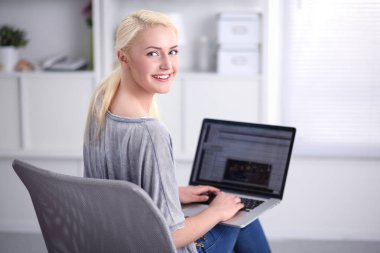 Genç ve güzel bir kadın evde dizüstü bilgisayar kullanıyor.