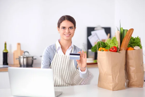 Lachende vrouw online winkelen met behulp van computer en creditcard in de keuken — Stockfoto