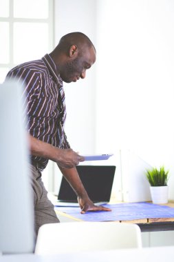 Ofiste bilgisayar ve planlarla çalışan Afrikalı Amerikalı bir mimar.