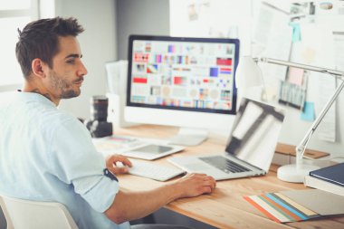 İnternette çalışırken bilgisayarın ve dizüstü bilgisayarın önünde grafik stüdyosunda oturan genç tasarımcının portresi.