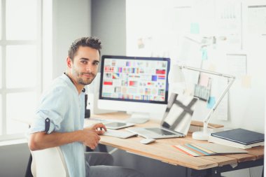 İnternette çalışırken bilgisayarın ve dizüstü bilgisayarın önünde grafik stüdyosunda oturan genç tasarımcının portresi.