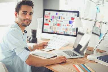 İnternette çalışırken bilgisayarın ve dizüstü bilgisayarın önünde grafik stüdyosunda oturan genç tasarımcının portresi.