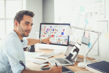 İnternette çalışırken bilgisayarın ve dizüstü bilgisayarın önünde grafik stüdyosunda oturan genç tasarımcının portresi.