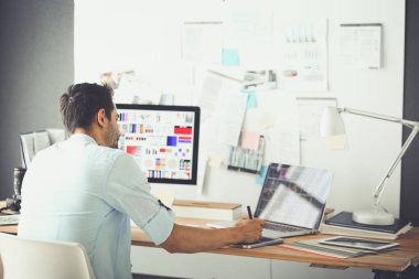 İnternette çalışırken bilgisayarın ve dizüstü bilgisayarın önünde grafik stüdyosunda oturan genç tasarımcının portresi.