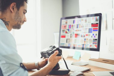 İnternette çalışırken bilgisayarın ve dizüstü bilgisayarın önünde grafik stüdyosunda oturan genç tasarımcının portresi.