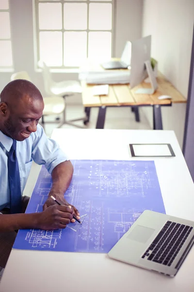 Afrikanischer Architekt arbeitet mit Computer und Bauplänen im Büro — Stockfoto