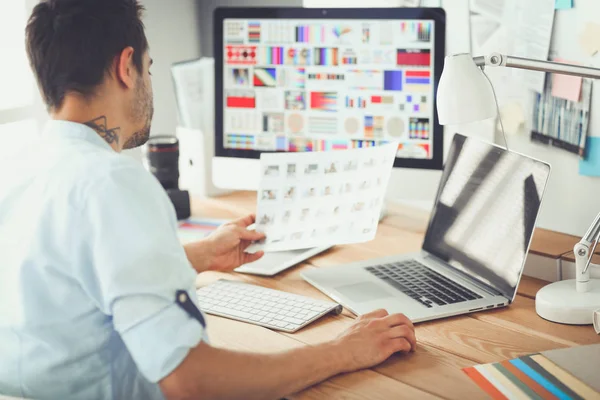 İnternette çalışırken bilgisayarın ve dizüstü bilgisayarın önünde grafik stüdyosunda oturan genç tasarımcının portresi.