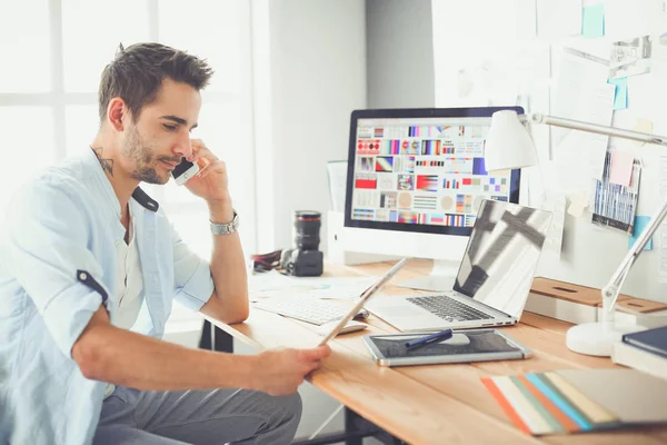 İnternette çalışırken bilgisayarın ve dizüstü bilgisayarın önünde grafik stüdyosunda oturan genç tasarımcının portresi.