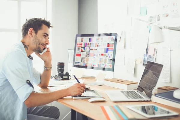 Retrato del joven diseñador sentado en el estudio gráfico frente a la computadora portátil y el ordenador mientras trabaja en línea. — Foto de Stock