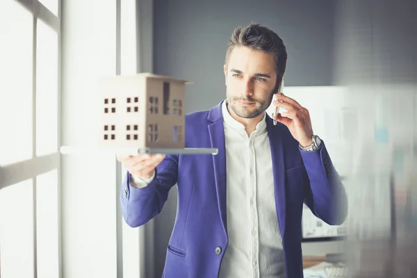 Homme d'affaires tenant maison miniature à portée de main debout dans le bureau . — Photo