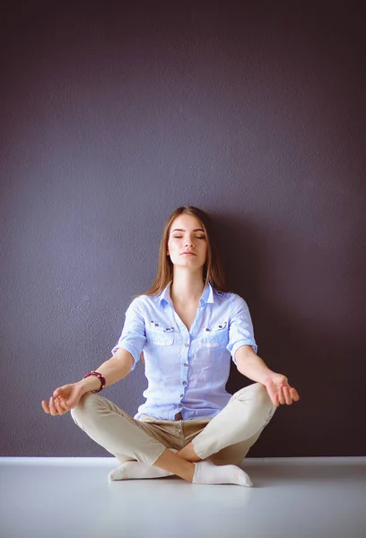 Portrait d'une femme heureuse décontractée assise sur le sol sur fond gris — Photo