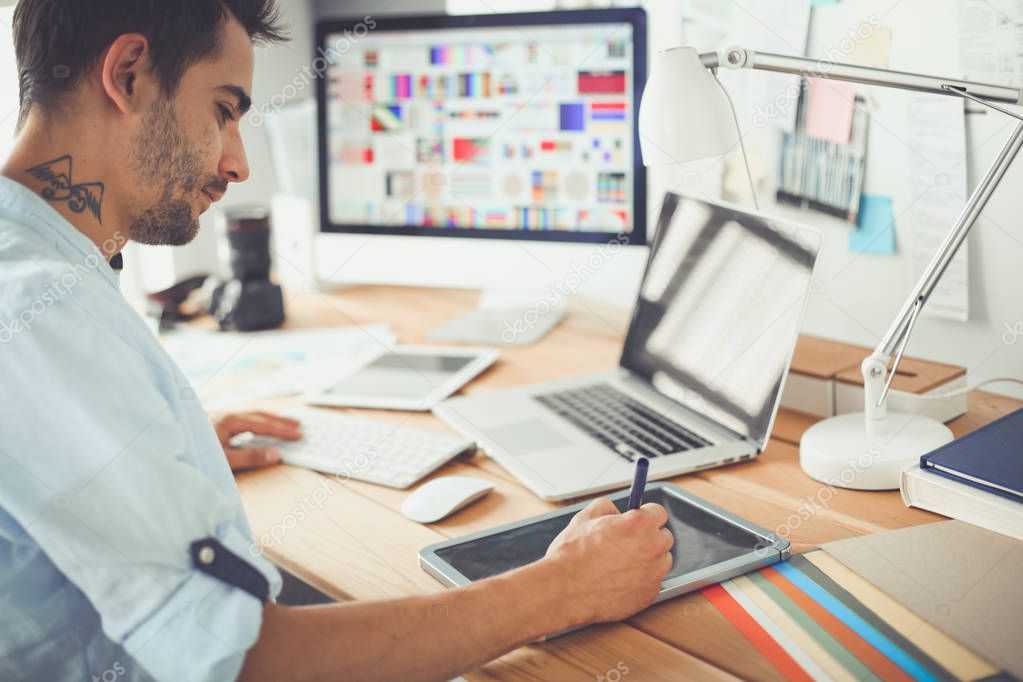 Portrait of young designer sitting at graphic studio in front of laptop and computer while working online.