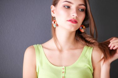 Gri duvarda gülümseyen genç bir kadının portresi.