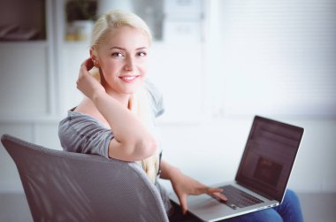 Genç ve güzel bir kadın evde dizüstü bilgisayar kullanıyor.