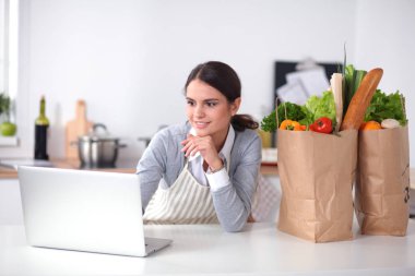 Mutfakta bilgisayar ve kredi kartı kullanan gülümseyen bir kadın.