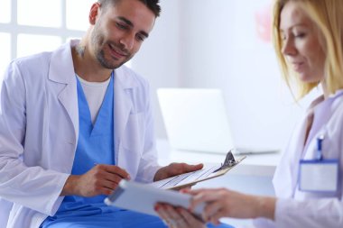 Yakışıklı doktor genç bayan hastasıyla konuşuyor ve ofisinde otururken notlar alıyor.