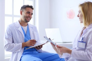 Yakışıklı doktor genç bayan hastasıyla konuşuyor ve ofisinde otururken notlar alıyor.