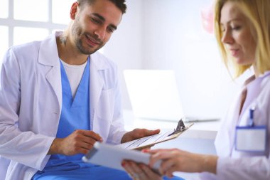 Yakışıklı doktor genç bayan hastasıyla konuşuyor ve ofisinde otururken notlar alıyor.