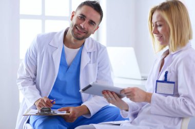 Yakışıklı doktor genç bayan hastasıyla konuşuyor ve ofisinde otururken notlar alıyor.