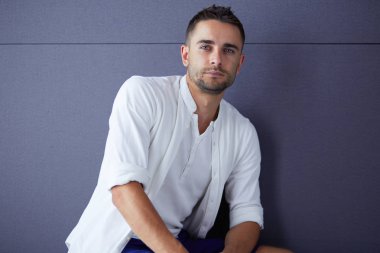 Gri arka planda yalnız oturan genç iş adamı