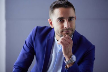 Gri arka planda yalnız oturan genç iş adamı